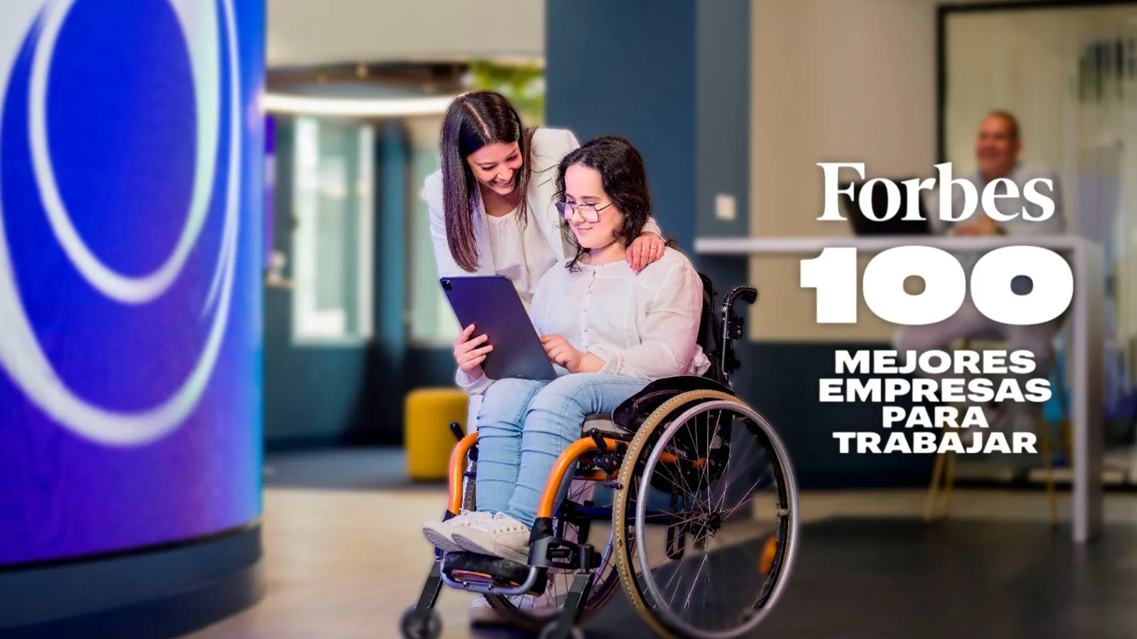 Cartela: Dos mujeres, una de ellas utiliza silla de ruedas, leen juntas un documento. Al lado, la leyenda: Forbes, 100 mejores empresas para trabajar