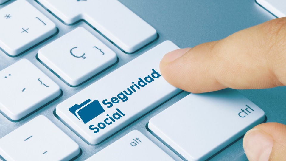 Un dedo presiona una tecla del teclado con la etiqueta "Seguridad Social", que presenta un icono de carpeta azul. La escena transmite acceso digital a la información de la seguridad social.