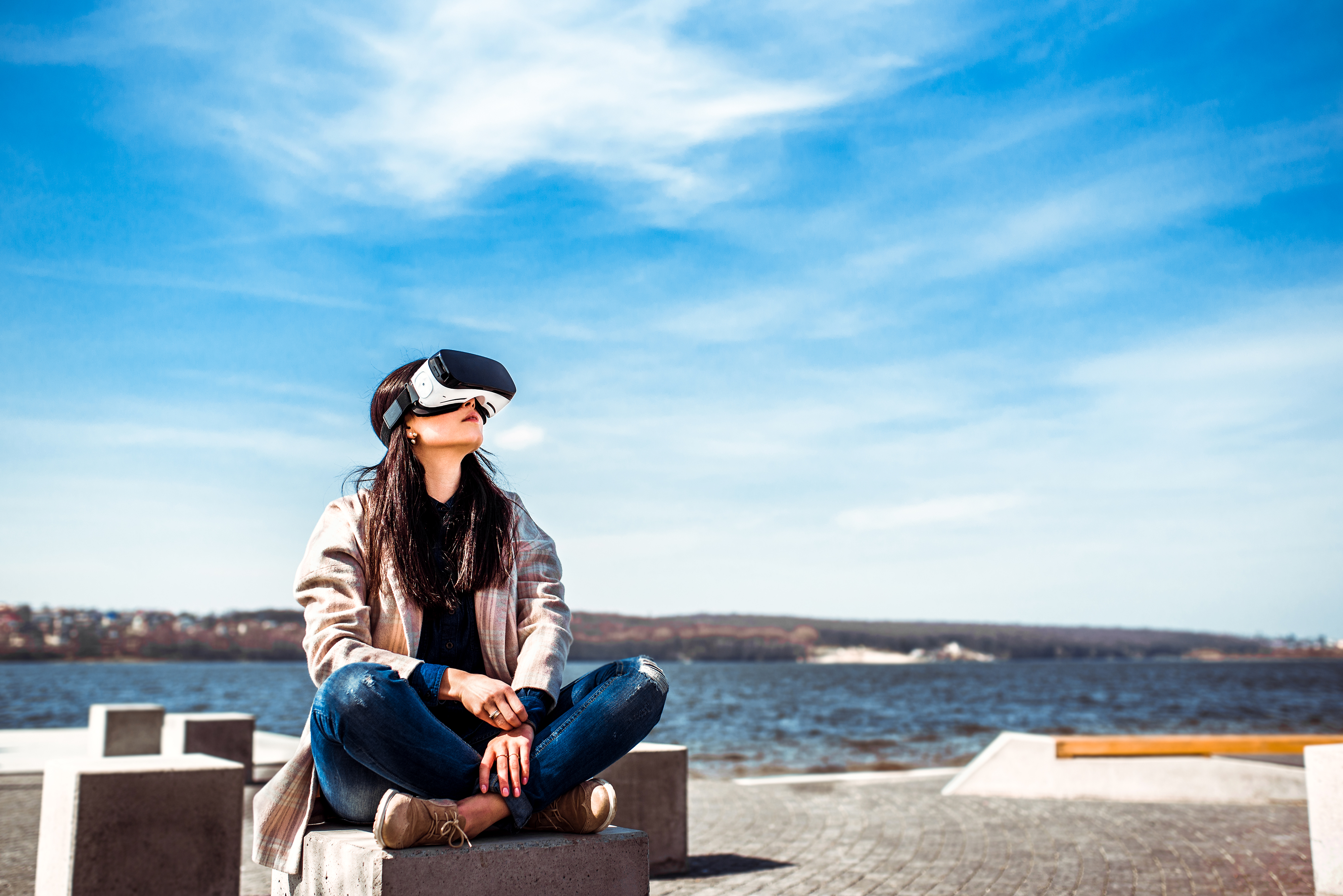 Una mujer joven en una playa con unas gafas de realidad virtual mirando hacia el cielo 