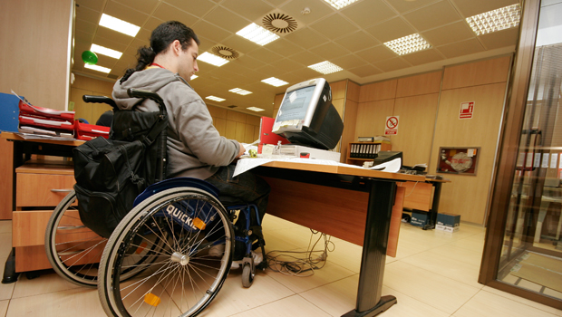 Imagen de un trabajador, usuario de silla de ruedas, en su mesa de despacho.