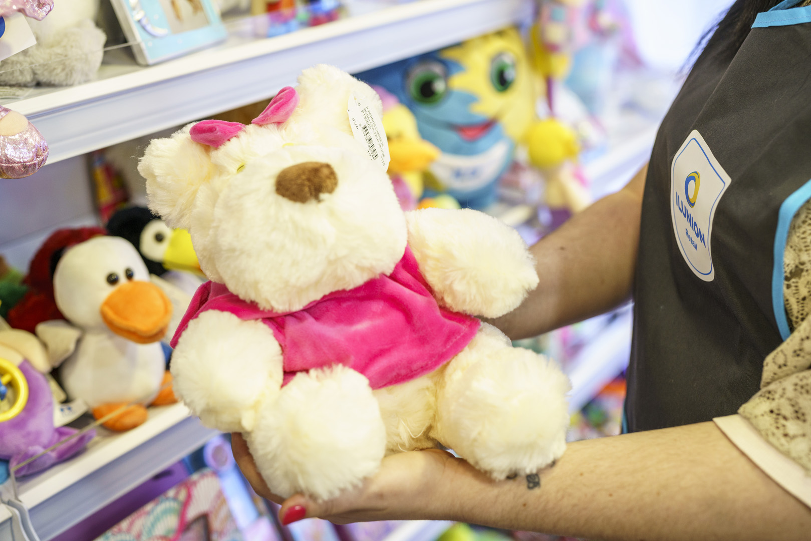Osito de peluche solidario sostenido por los brazos de una persona que trabaja en ILUNION Retail