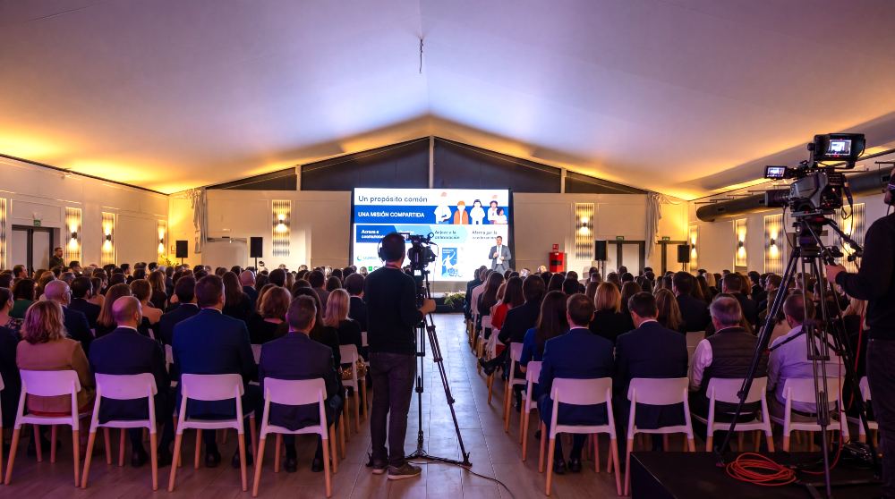 Evento corporativo con centenares asistentes sentados en sillas mirando a una pantalla led y el presentador