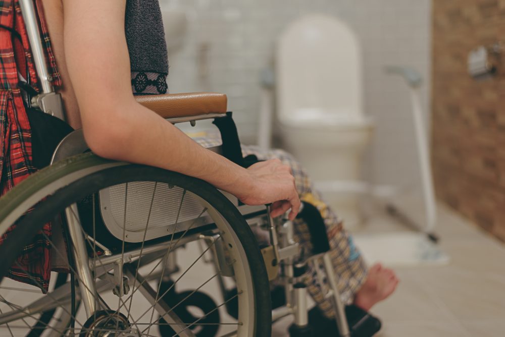 Persona sentada en silla de ruedas en un baño accesible, con barras de apoyo y sanitario al fondo