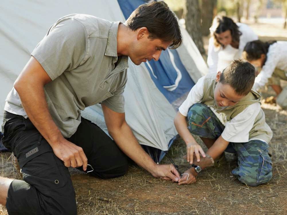 Personas montando una tienda de campaña en un entorno natural, fijando las piquetas al suelo durante una actividad de campamento