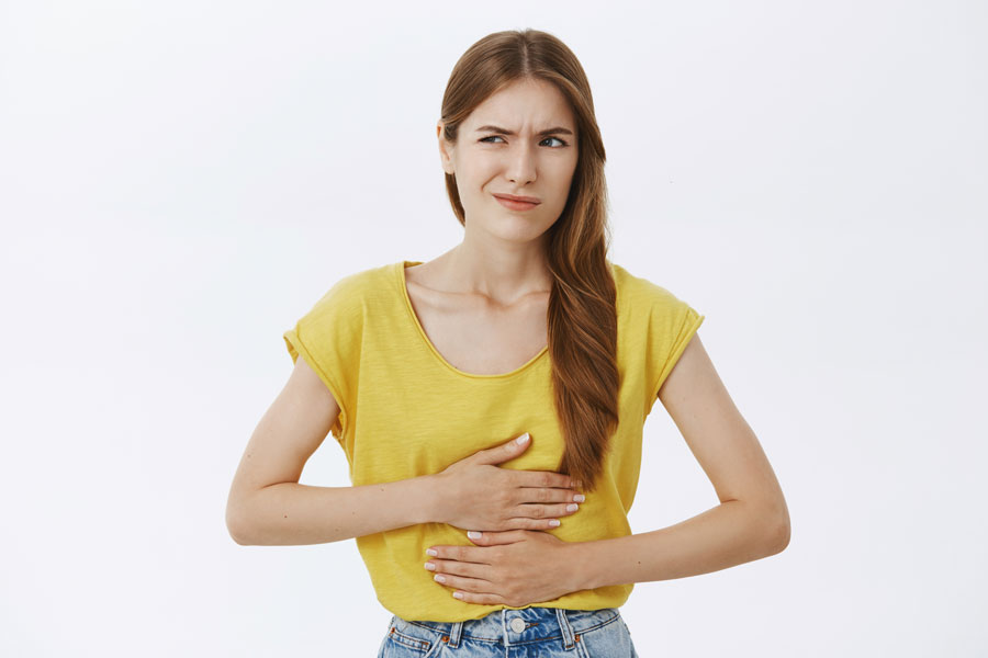 Mujer con camiseta amarilla muestra una expresión facial de malestar mientras se toca la barriga con las dos manos.