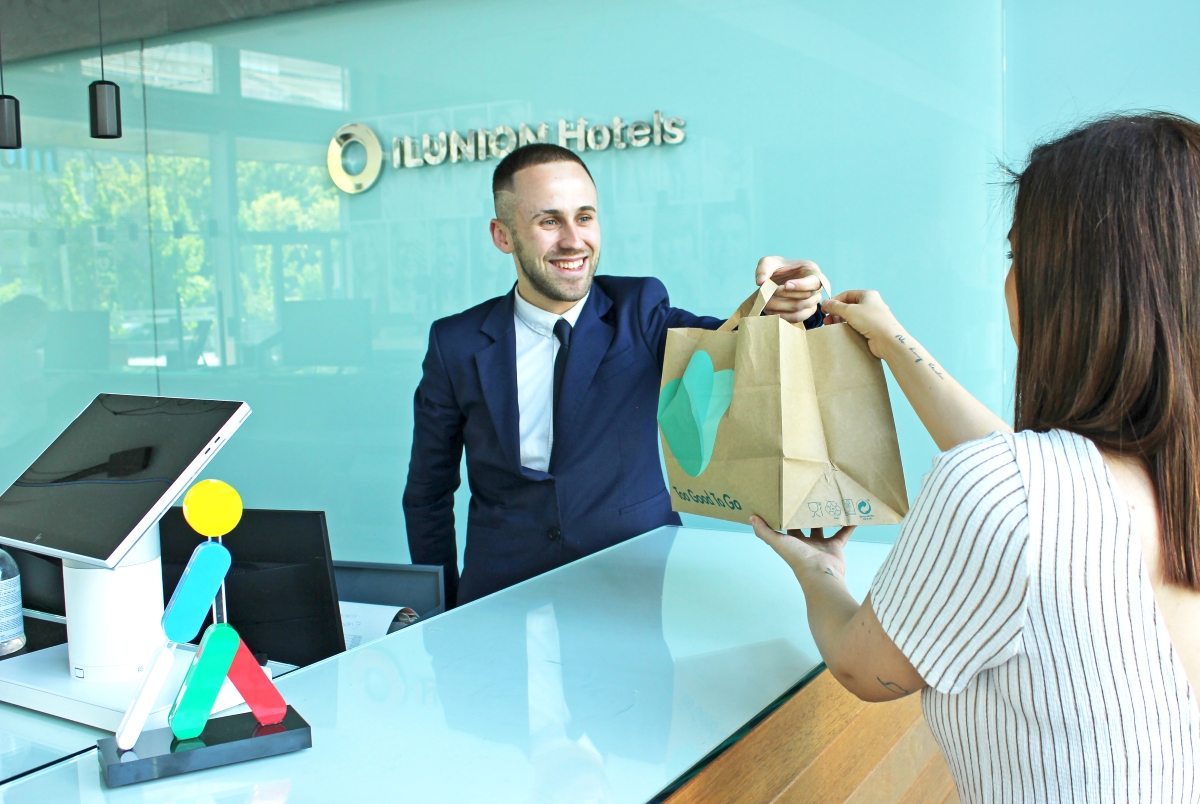 Un trabajador de ILUNION Hotels entrega una bolsa de papel con comida a una clienta