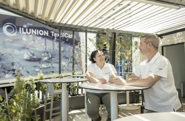Dos personas que trabajan en ILUNION TextilCare charlan en una zona con sol y plantas de la compañía