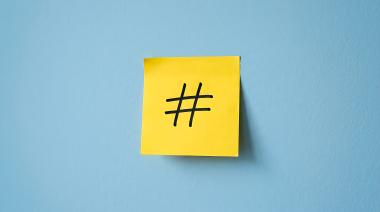 Un hashtag escrito en un post it amarillo pegado a una pared azul
