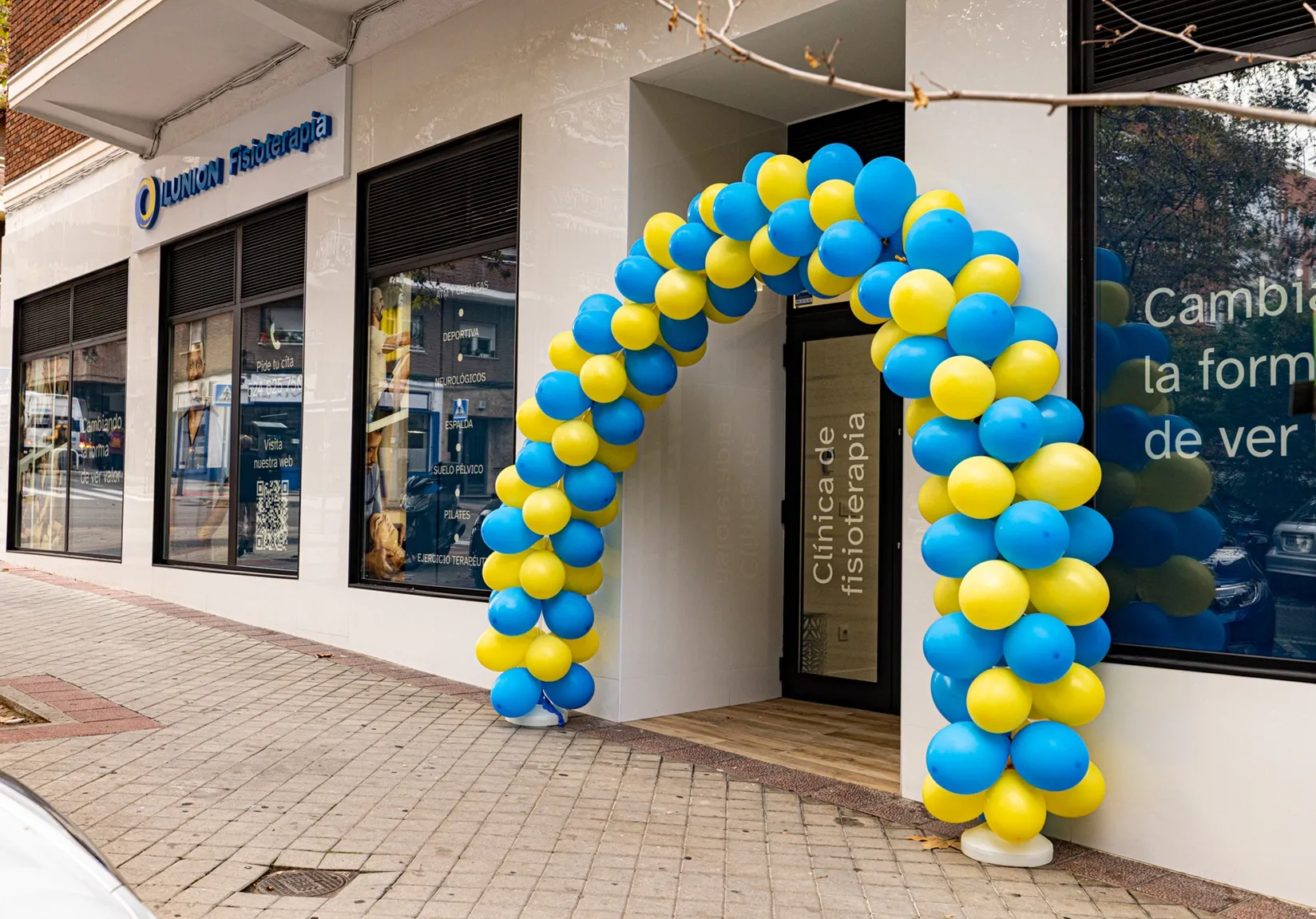 Entrada principal de la nueva clínica de fisioterapia de ILUNION en la madrileña calle de Pensamiento, decorada con un arco de globos con los colores corporativos del grupo empresarial, azul y amarillo