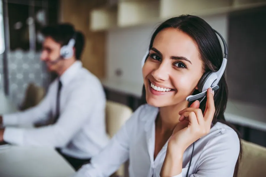 Dos personas trabajando en un centro de atención telefónica, usando auriculares con micrófono y vistiendo ropa formal, sentadas frente a ordenadores en un entorno de oficina