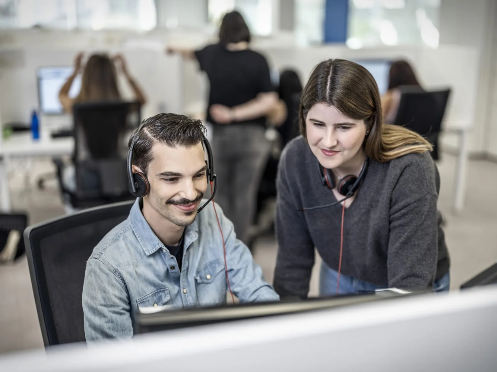 Una trabajadora de ILUNION Contact Center BPO atiende a un compañero en su puesto de trabajo