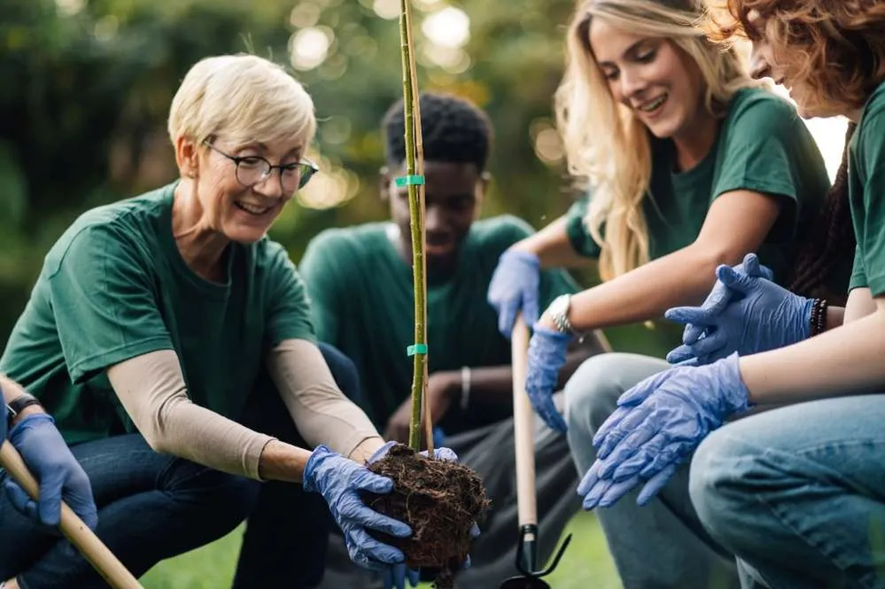 Voluntarios con camisetas verdes y guantes azules plantando un árbol