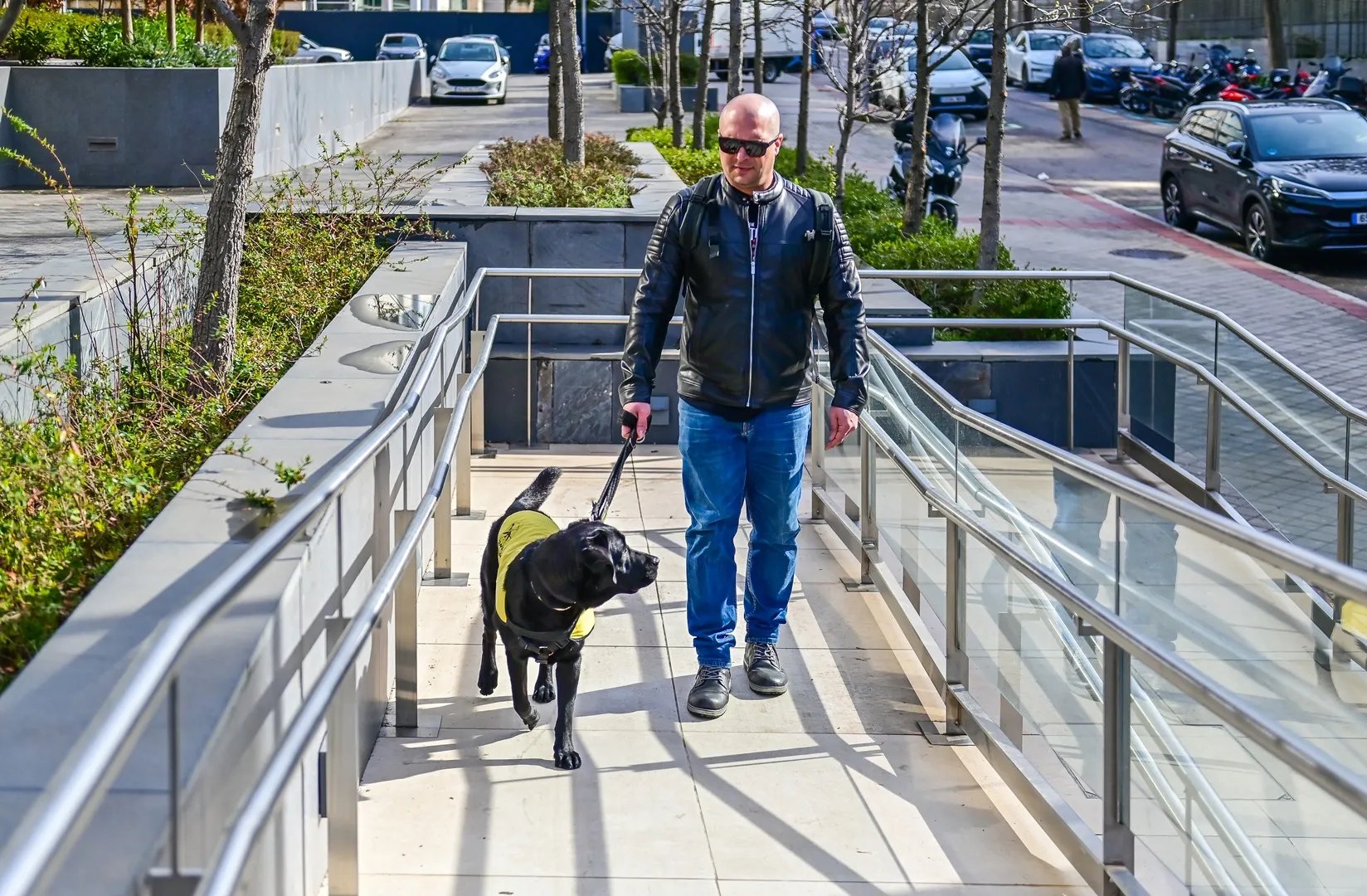 Un hombre con discapacidad visual accede, acompañado de su perro guía, por la rampa de acceso a un hotel ILUNION