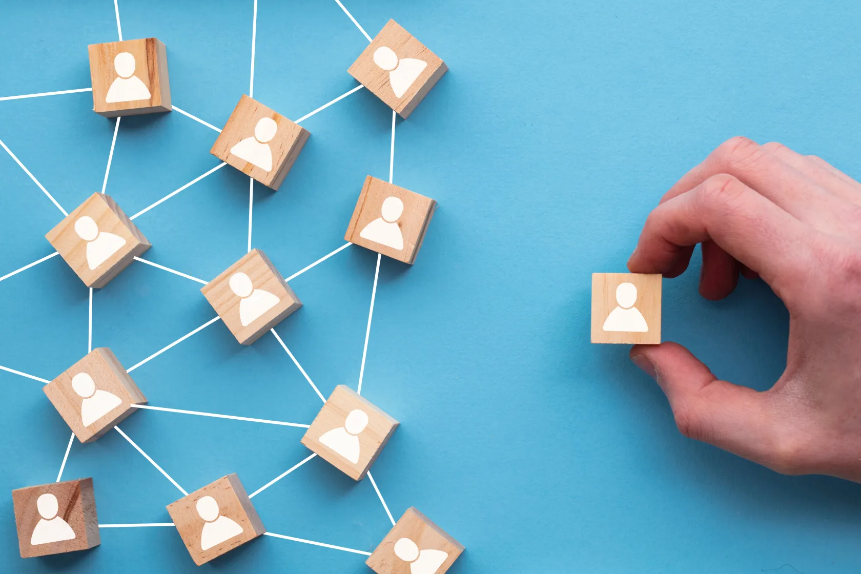 Bloques de madera con iconos de personas conectados por líneas, mientras una mano separa un bloque de la red.