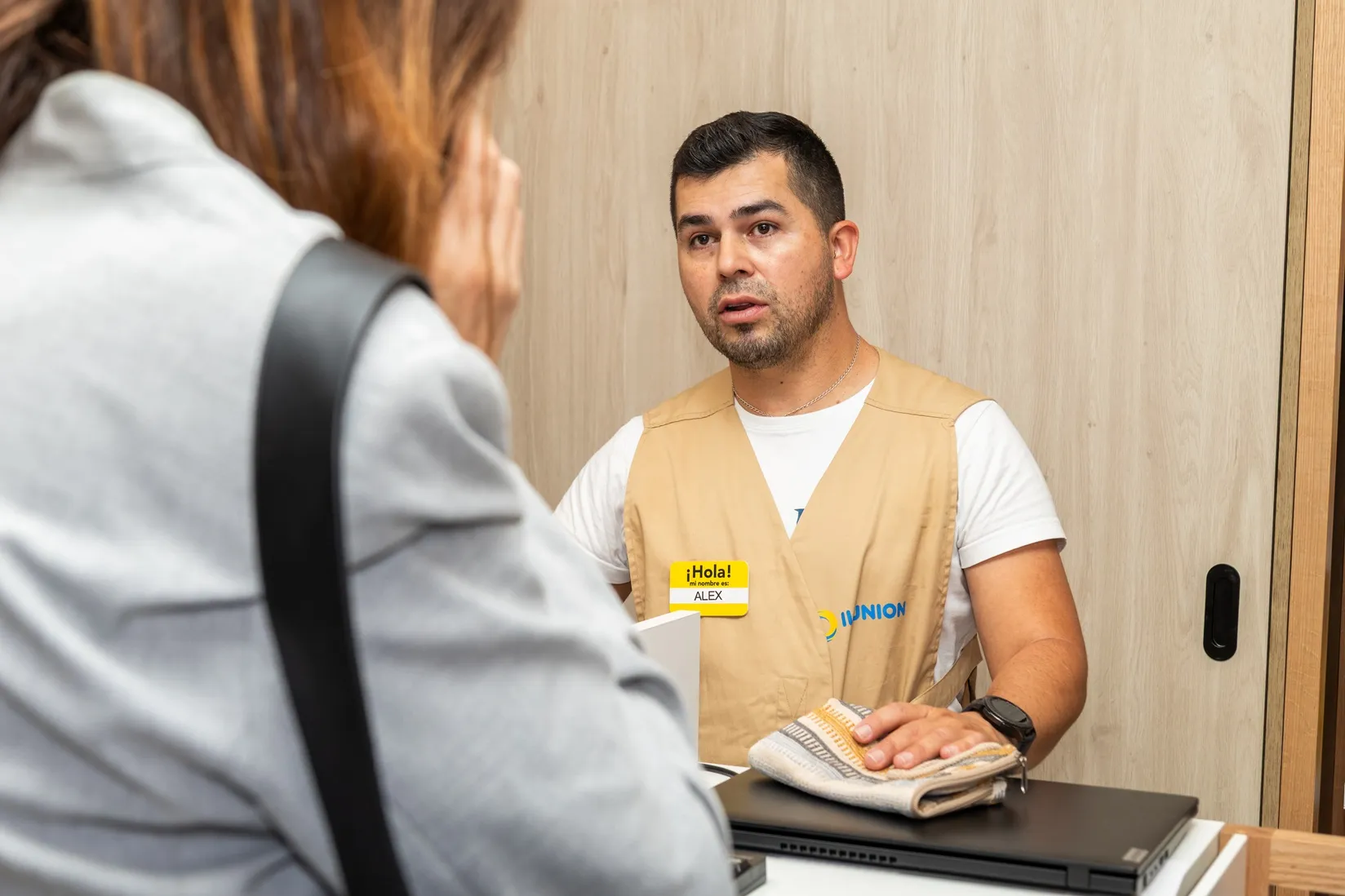 Uno de los trabajadores de la nueva tienda de ILUNION en el hospital de Sanitas en Valdedebas atiende a una clienta en caja