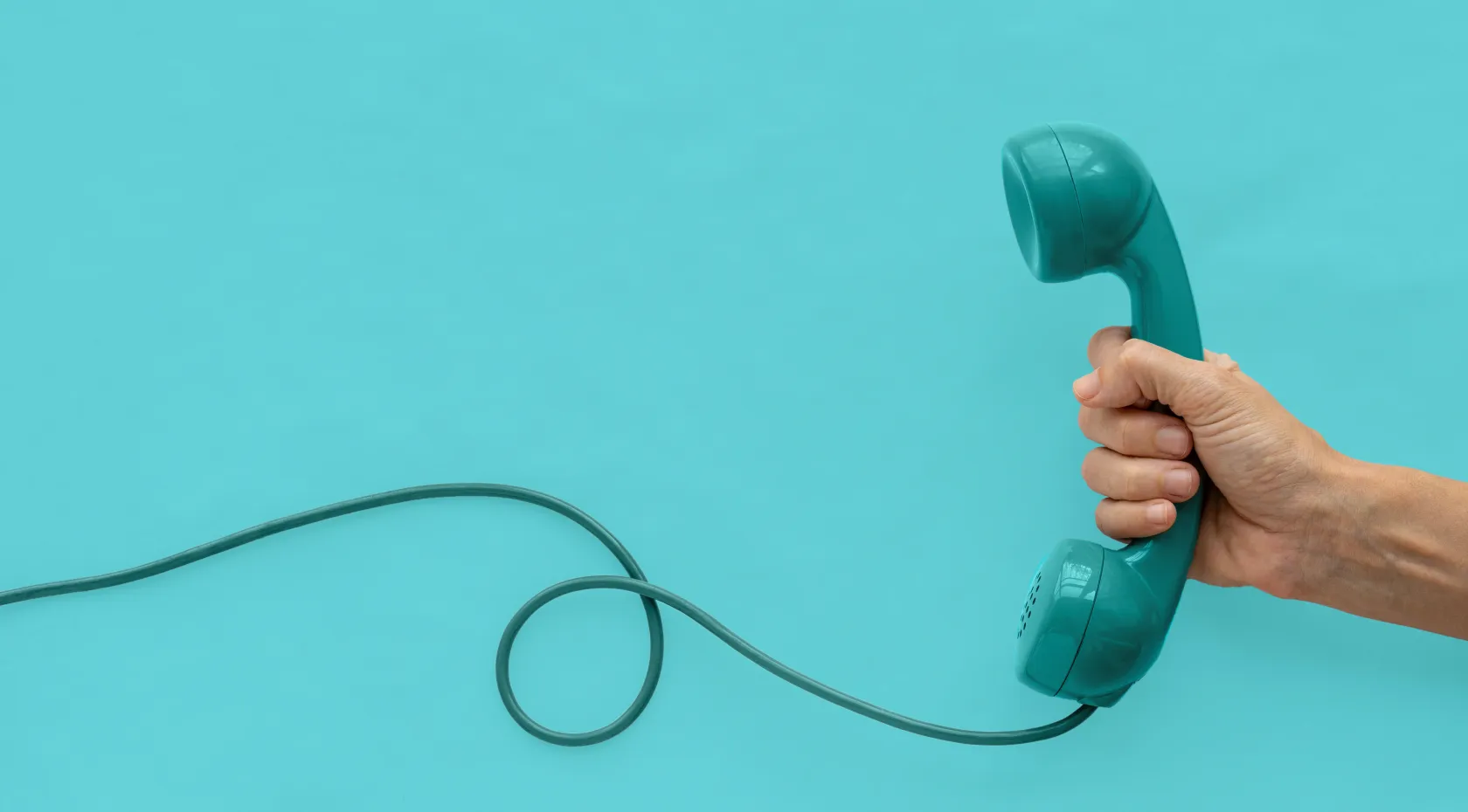 Mano sosteniendo un auricular de teléfono verde con cable enroscado sobre fondo azul.
