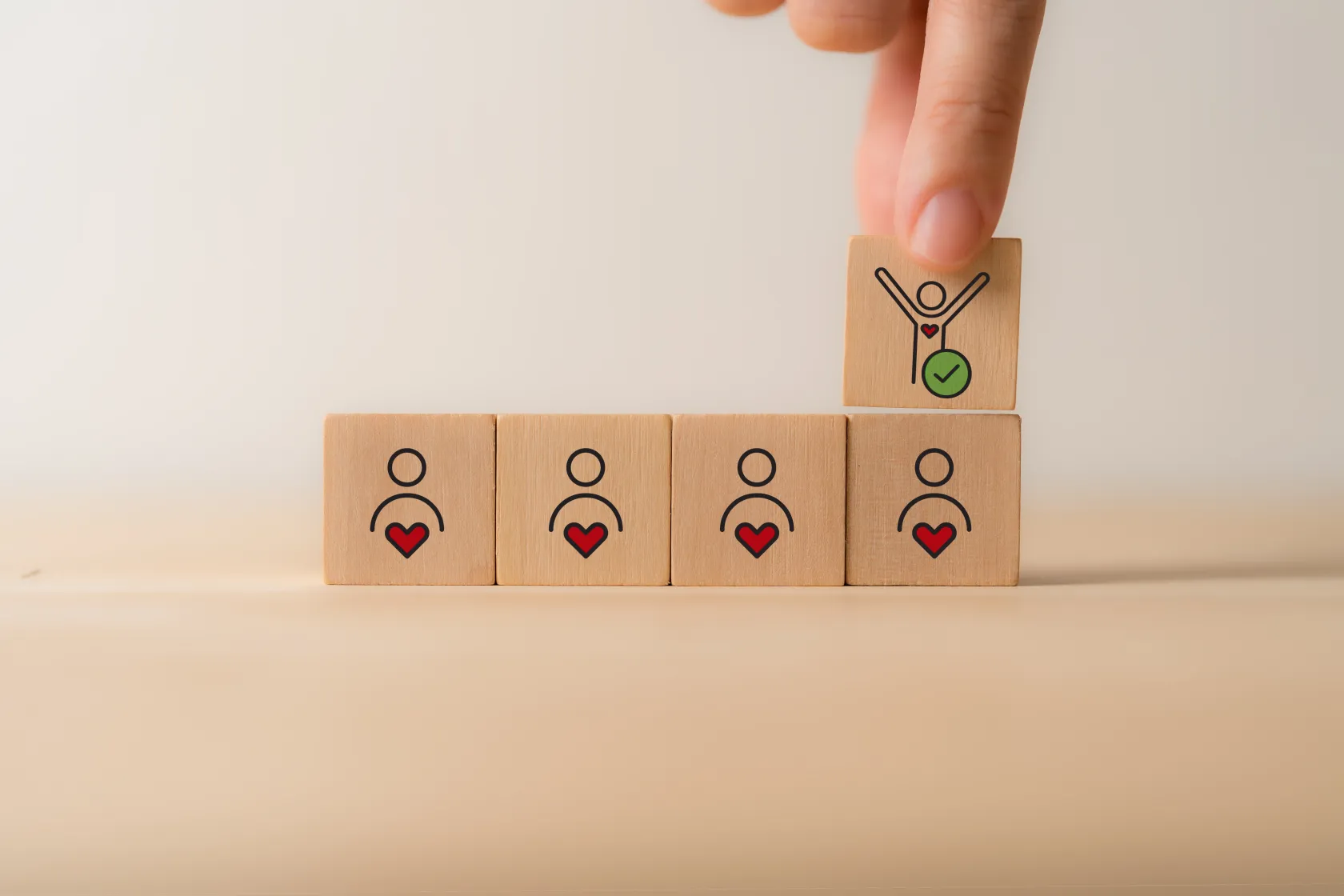 Bloques de madera con iconos de personas y corazones; una mano coloca un bloque con una figura y una marca de verificación, simbolizando inclusión o selección de talento