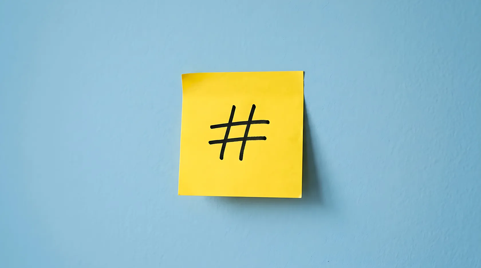 Un hashtag escrito en un post it amarillo pegado a una pared azul