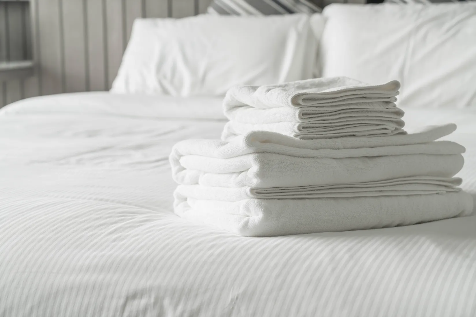 Toallas blancas dobladas sobre una cama de hotel con sábanas y almohadas blancas.