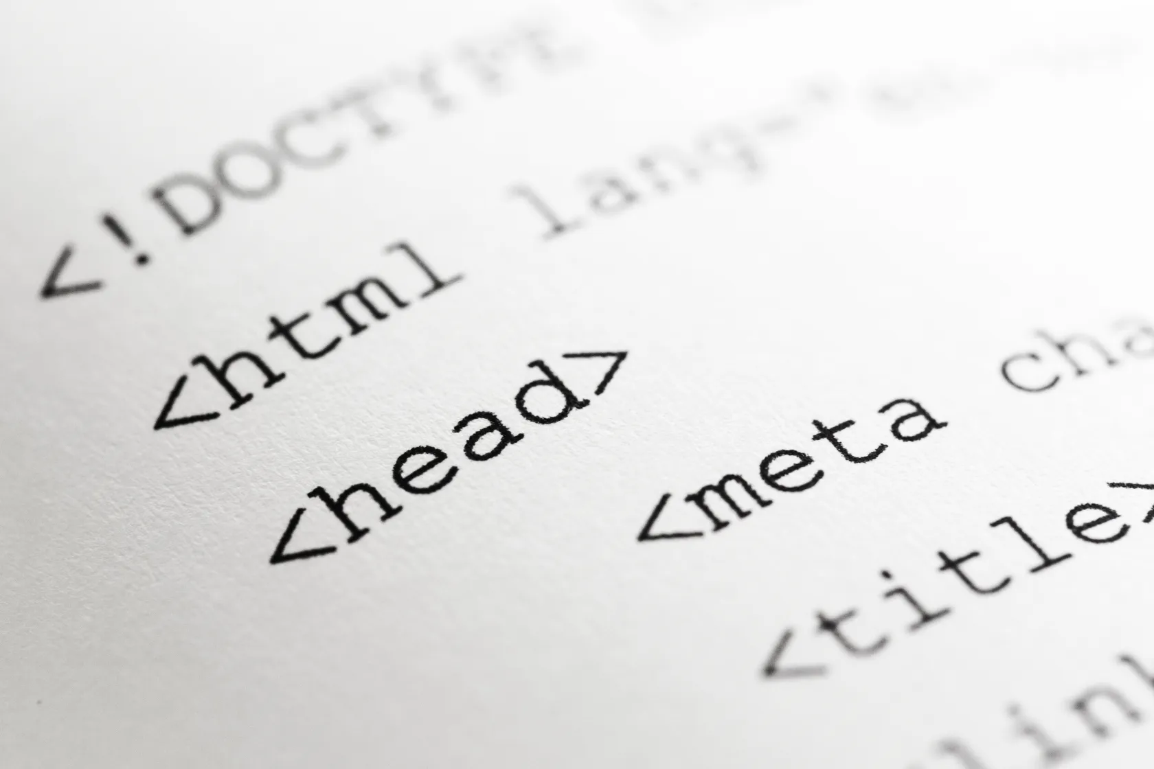 Detalle de código HTML impreso en papel, con etiquetas como “html”, “head” y “meta” destacadas en primer plano