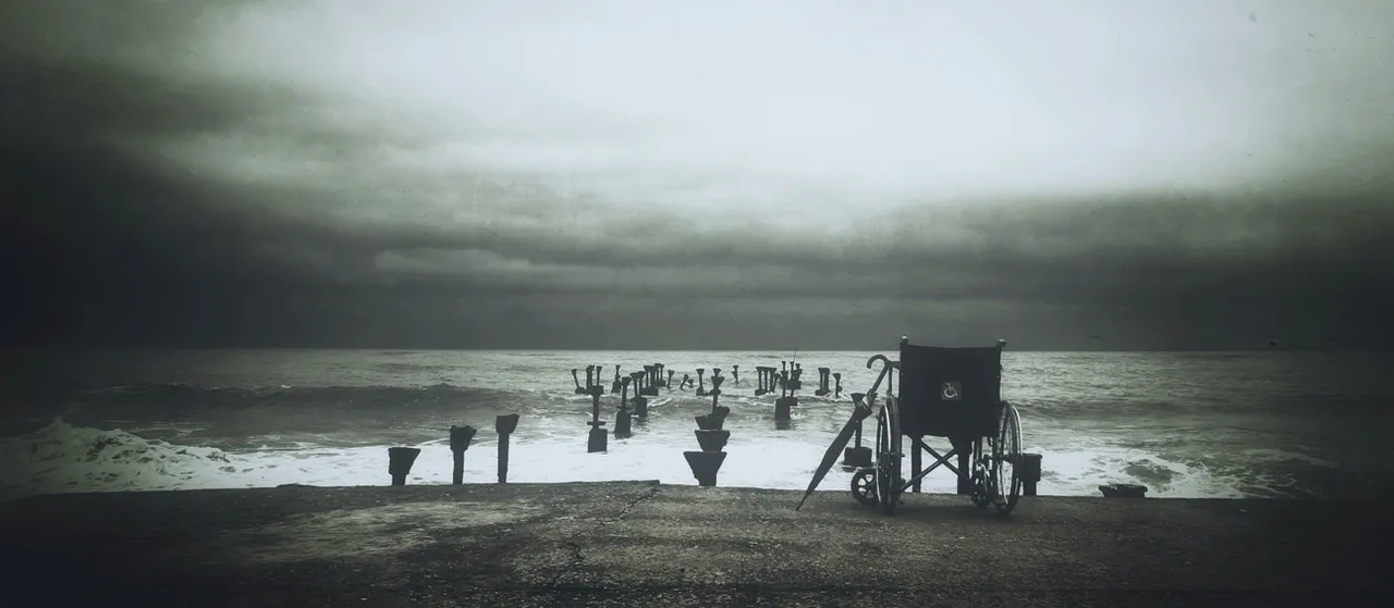 Imagen en blanco y negro donde se ve una silla de ruedas frente al mar