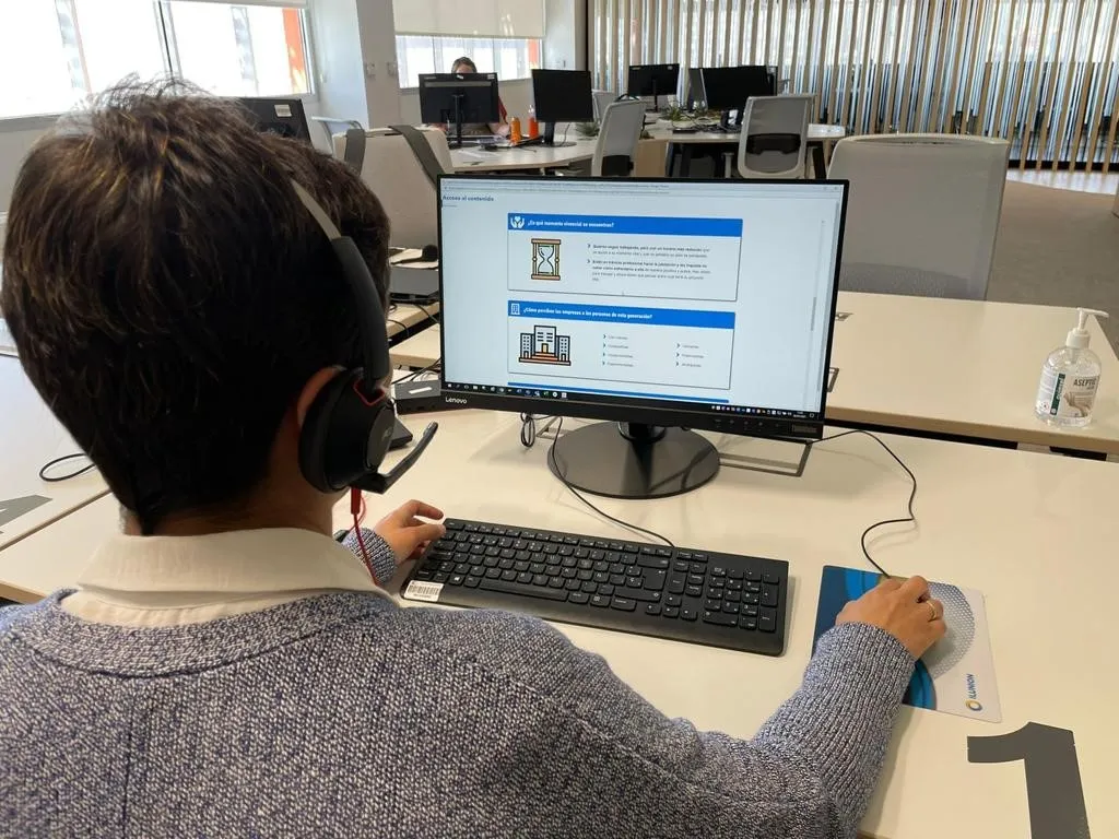 Una mujer de espaldas frente a la pantalla de un ordenador realiza un curso online