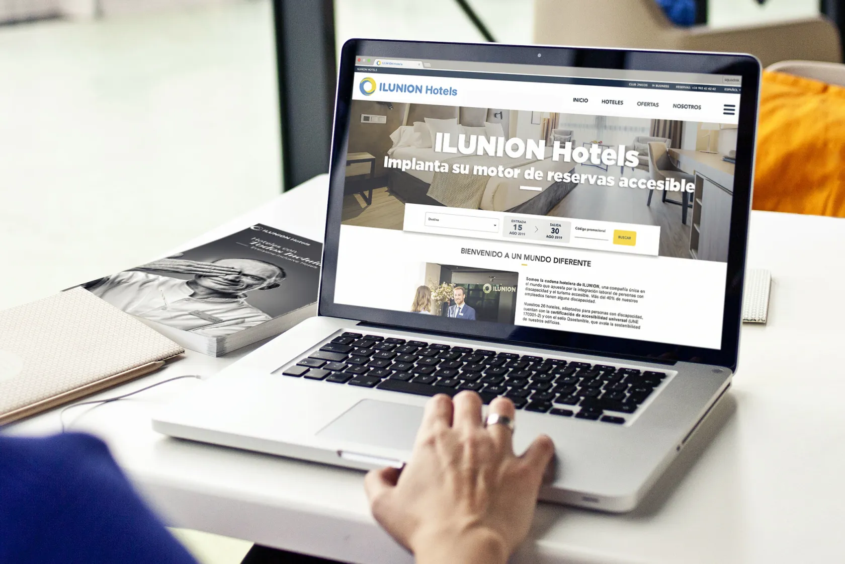 Imagen de la página web de ILUNION Hotels en una pantalla de ordenador portátil. Además, a la izquierda de la fotografía aparece el libro de 'Hoteles con Todos Incluidos'
