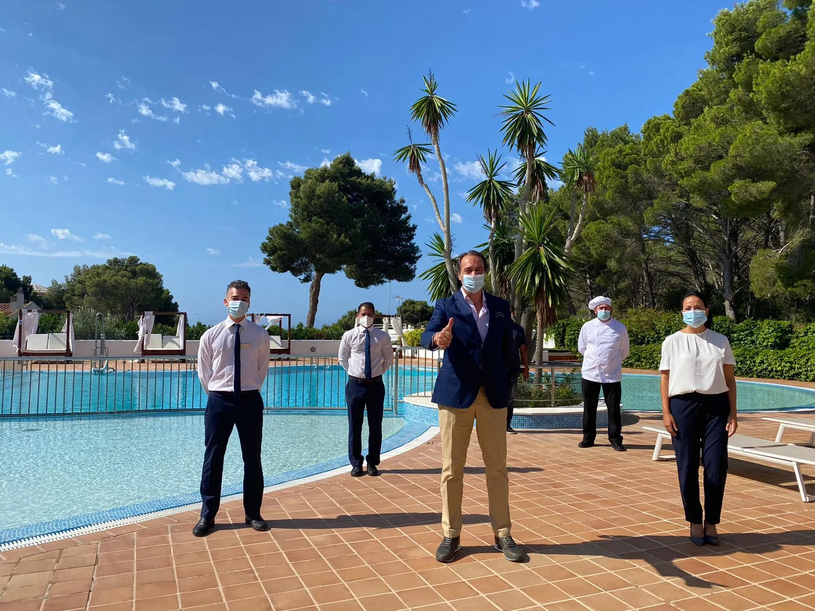 Imagen de los trabajadores del ILUNION Menorca en el exterior del hotel, manteniendo las distancias de seguridad y con sus EPI 