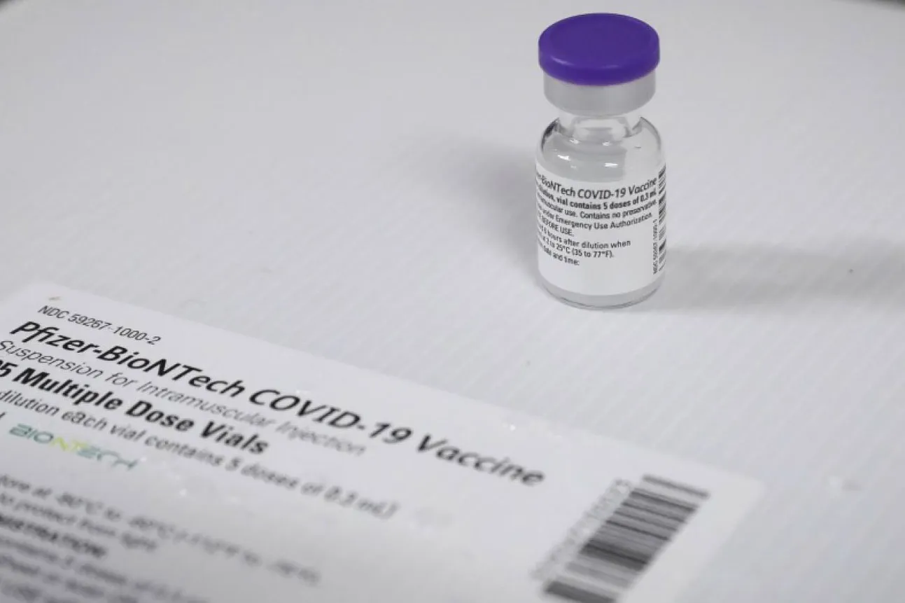 Fotografía de un vial de la vacuna de Pfizer junto a un papel con indicaciones 